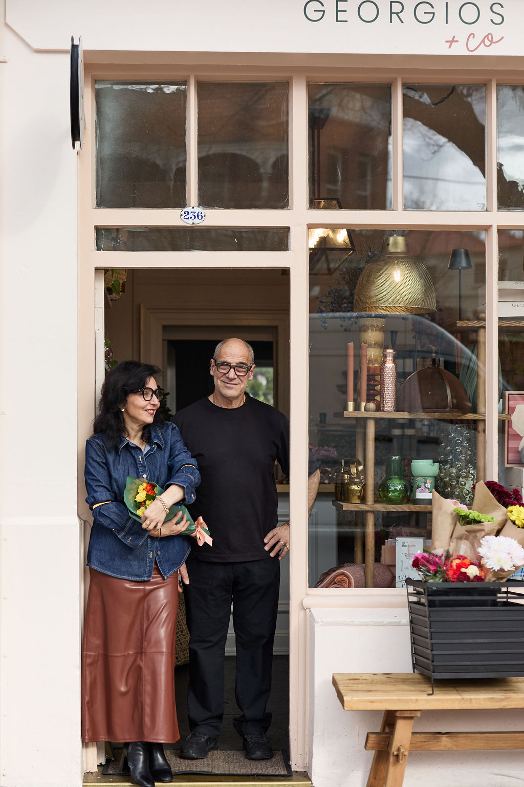 Two people standing in front of a store named 'Georgios & Co'.